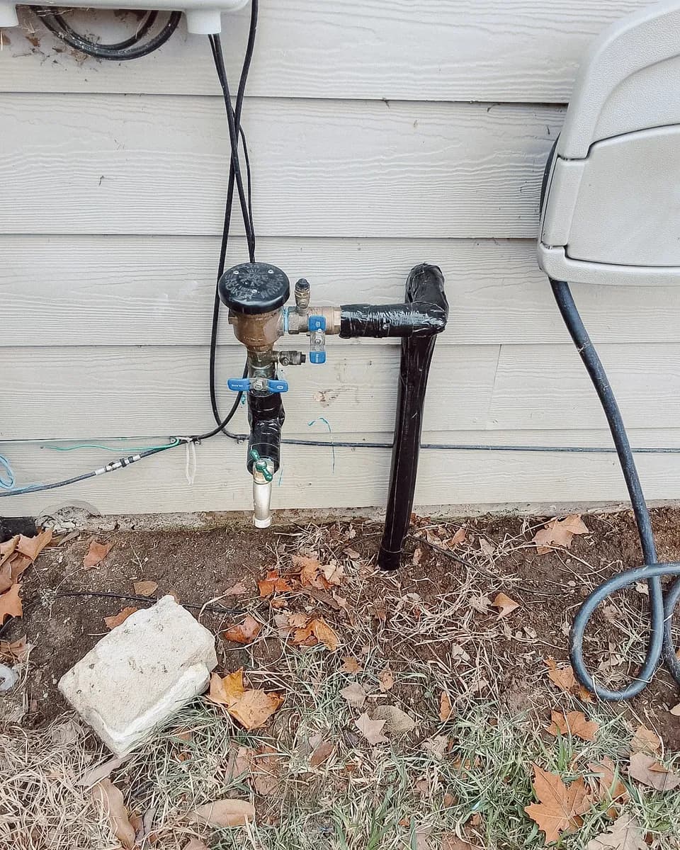 New brass irrigation backflow preventer with fresh insulated piping on the same wall