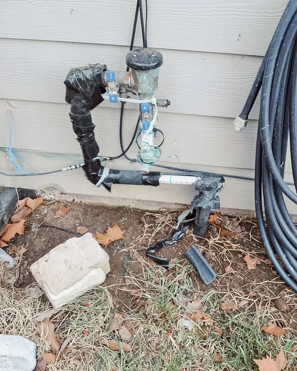 Old irrigation backflow preventer with taped, damaged pipe insulation and broken pieces on the ground