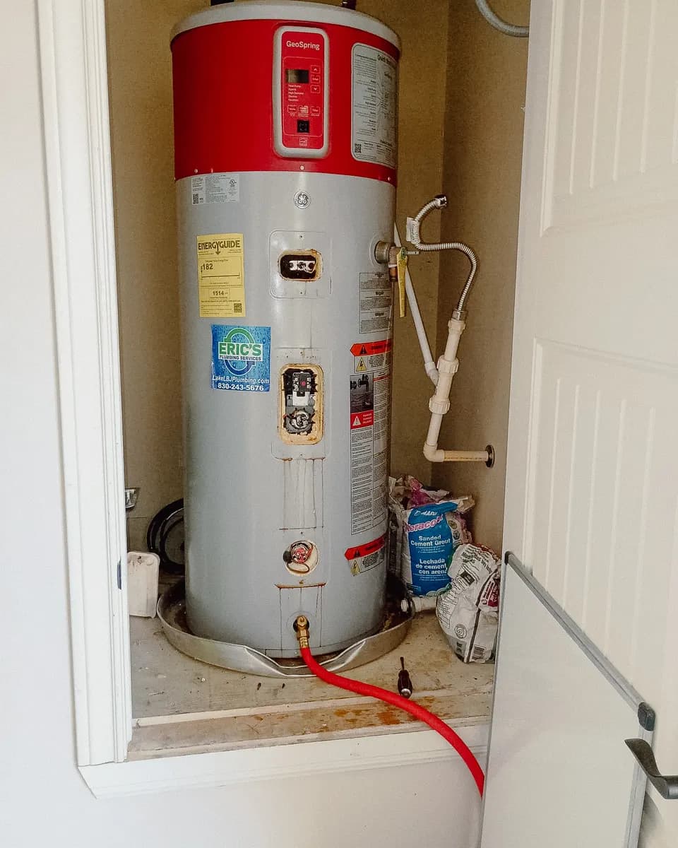 Old heat pump water heater being drained in a utility closet